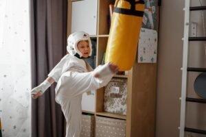 cute caucasian boy kicking a punchbag practicing karate at home